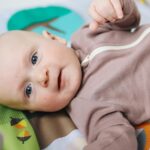 A cute baby lying on a colorful activity mat, engaging with soft toys overhead.