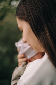 A mother lovingly holds her newborn close outdoors, symbolizing warmth and care.