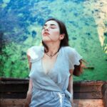 Young woman in a soft blue dress enjoys a tranquil moment by the river, embodying summer serenity.