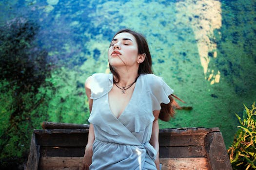 Young woman in a soft blue dress enjoys a tranquil moment by the river, embodying summer serenity.