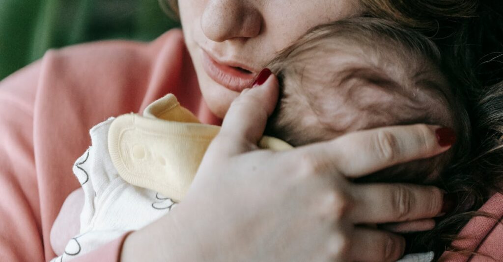 Upset mother with little newborn baby in arms looking into distance with serious gaze while standing in light room at home